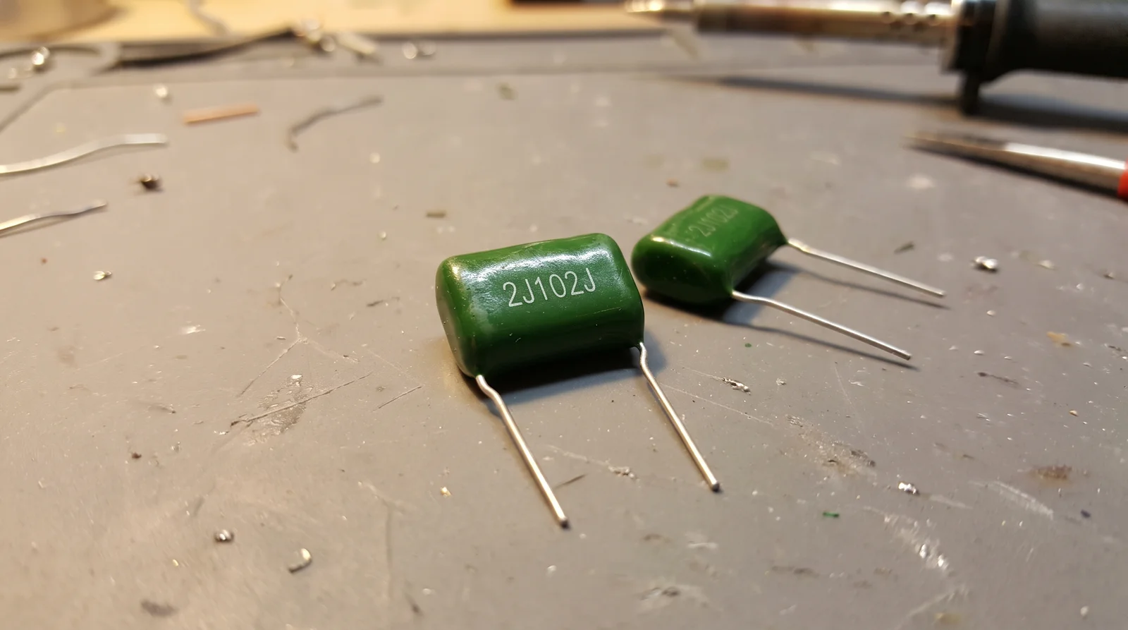 capacitor markings - green CL11 polyester film capacitor printed with the code 2J102J on a workbench